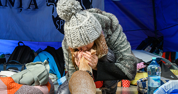 Photo by Narcis Pop, Speranta A woman crouches down while kissing her small tan dog on the head.
