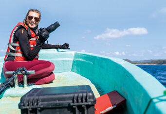Happy marine biologist working while taking photo sitting at the edge of a boat