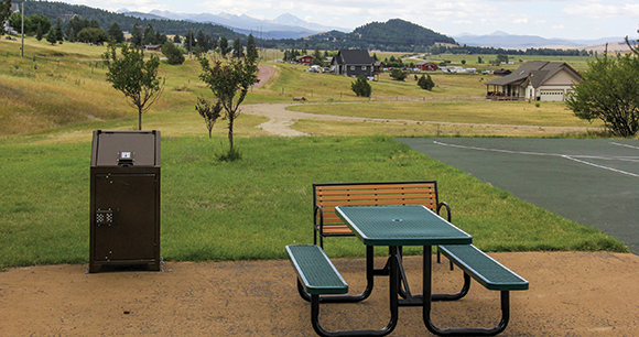 a picnic table and trash can near a park