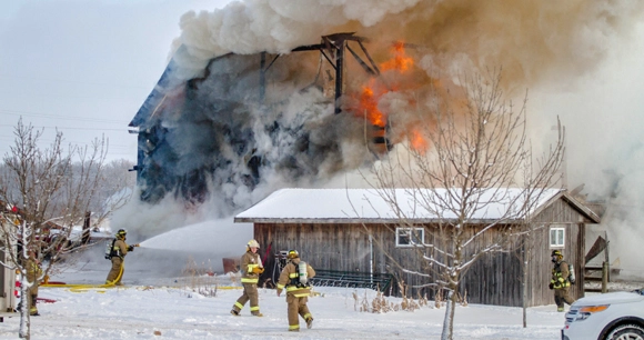 barn burning in snowy setting with firefighters in foreground using a hose