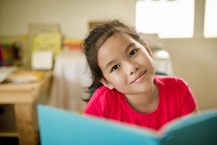 child looks up from reading book to smile
