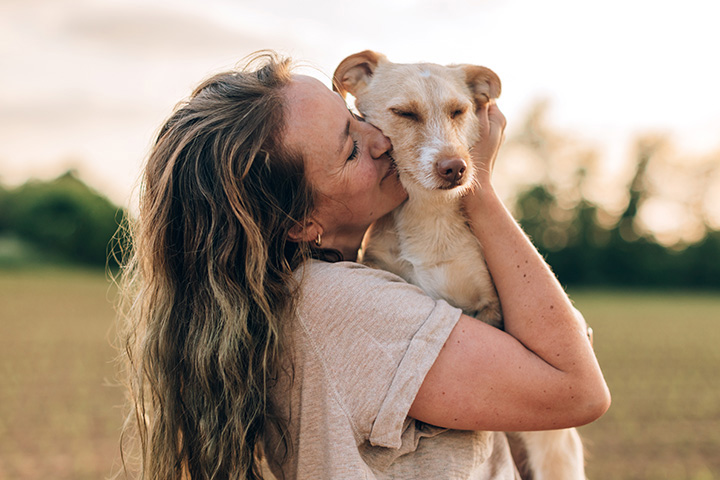 woman standing and embracing her dog lovingly on a field